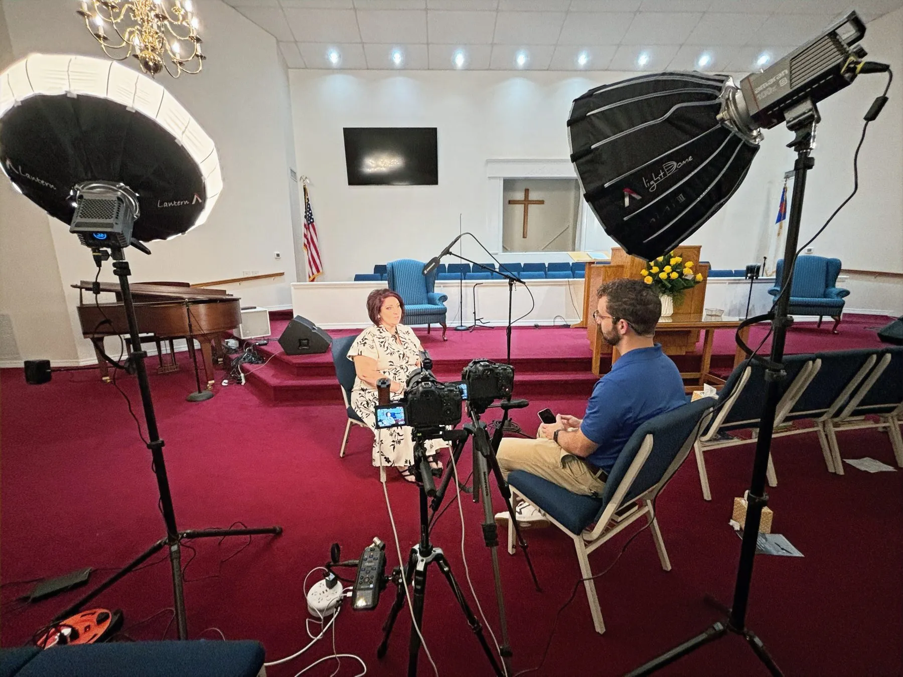 A video interview set up in a church sanctuary with studio lights and cameras.