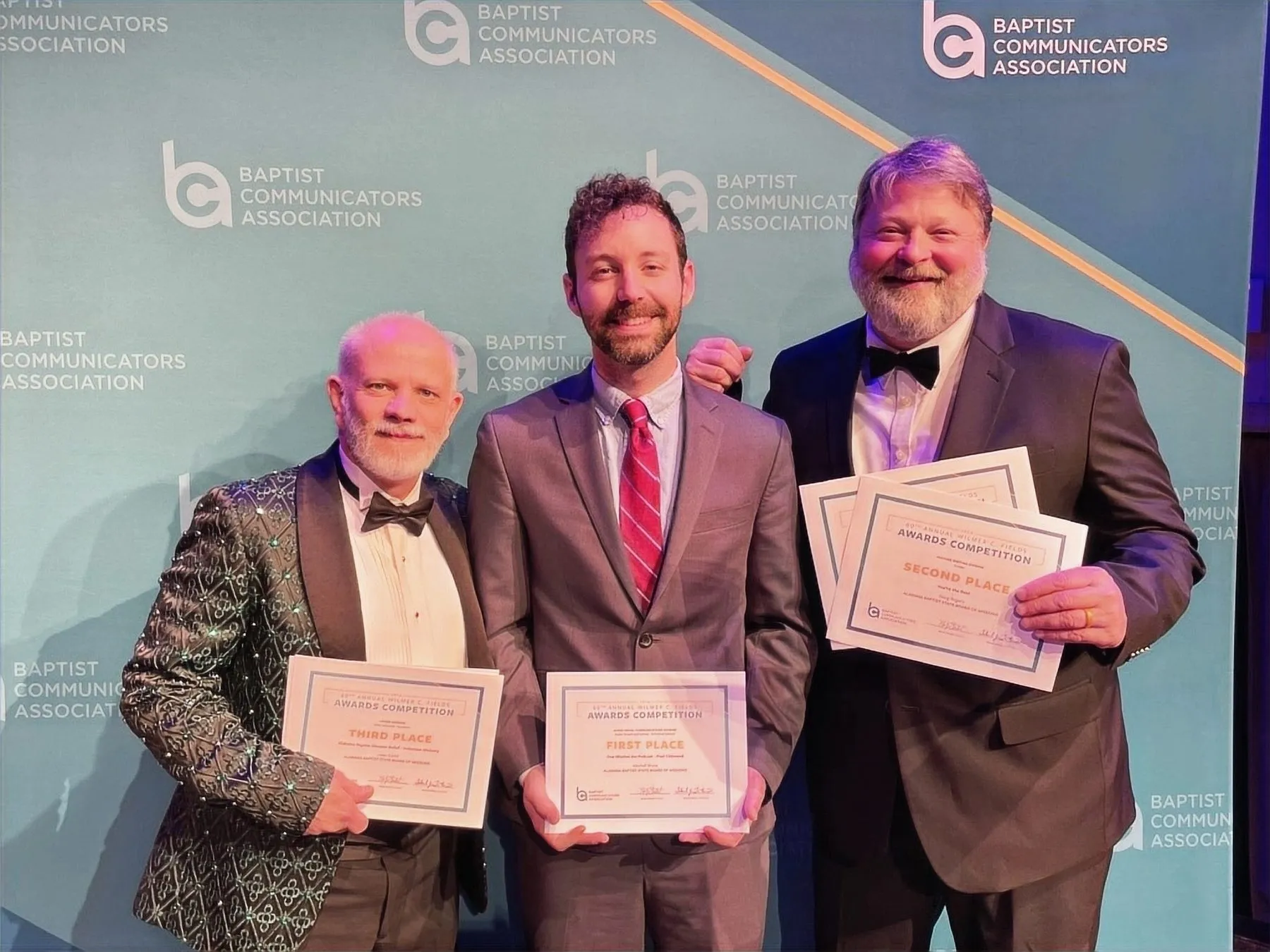 Three men in formal wear holding award certificates at the Baptist Communicators Association awards.