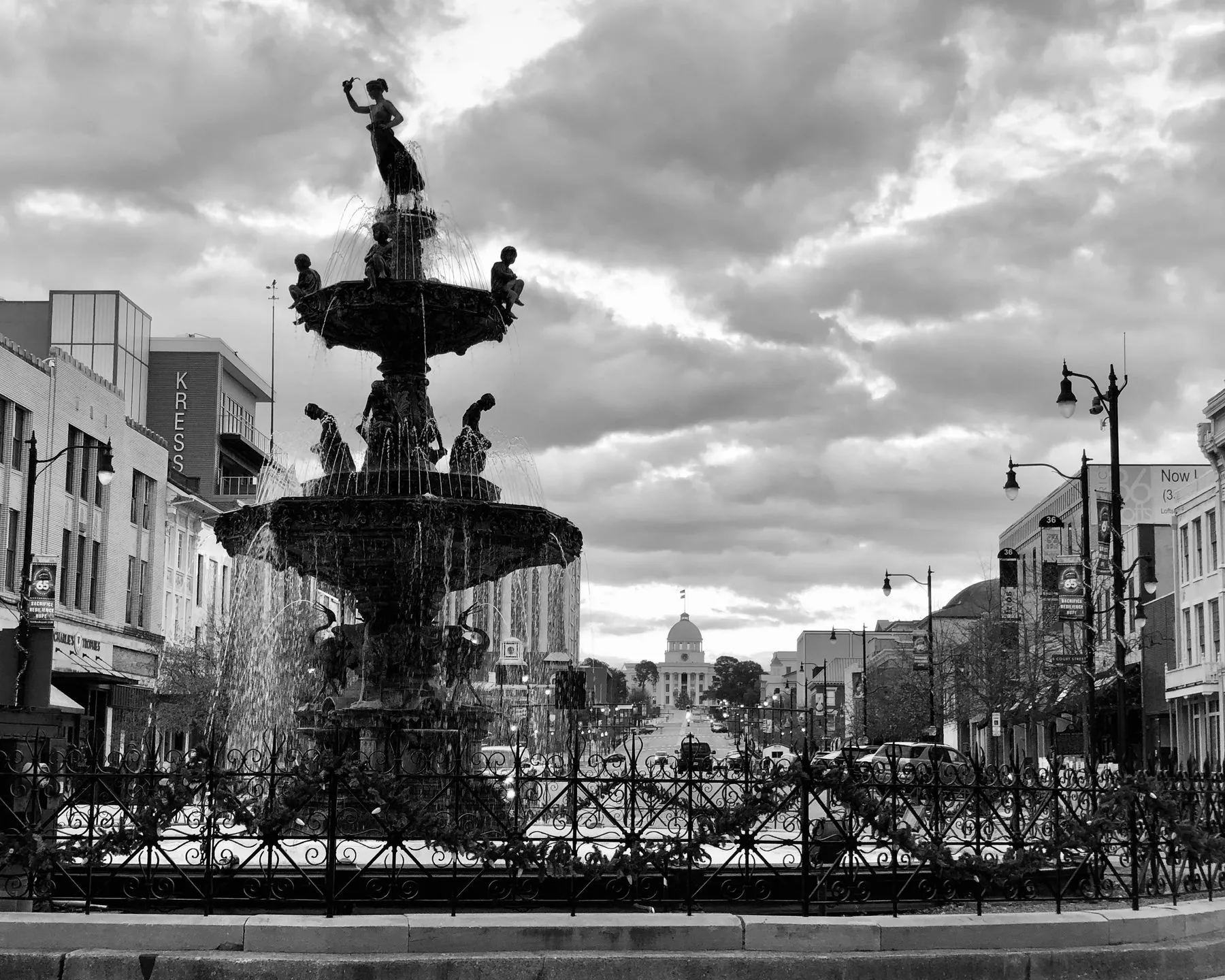 A black-and-white photo of an ornate fountain in a town square.