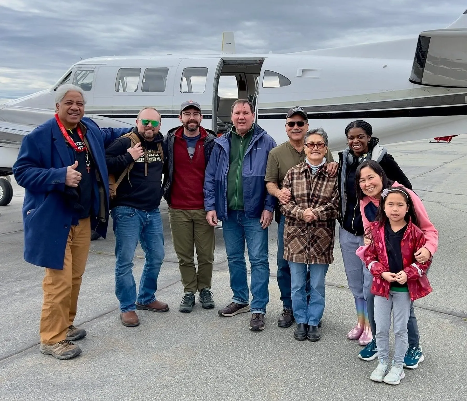 A group of people smiling in front of a small airplane.